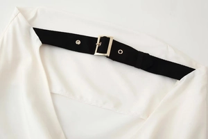 Close-up of white dress bodice with black strap and golden buckle detail