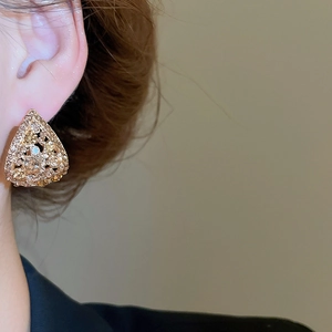 Close-up of golden hollow triangle earrings with amber and clear rhinestones on model