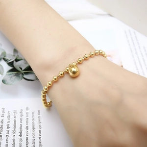 Detail of a gold-beaded bracelet with a sphere pendant worn on wrist with leaf decor