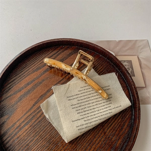 Detail of a golden metal hair claw clip with amber resin accent on a wooden display
