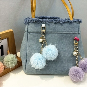Detail of light blue denim tote bag with yellow handle and plush fur ball pendants
