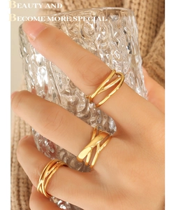 Three stacked gold-tone C-shaped multi-layered rings shown on a hand holding a glass cup