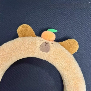 Close-up of plush Capybara headband with orange detail and soft brown fabric