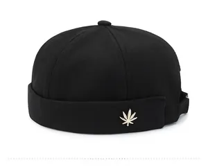Detail of black cotton docker cap featuring a gold maple leaf metal badge on the side