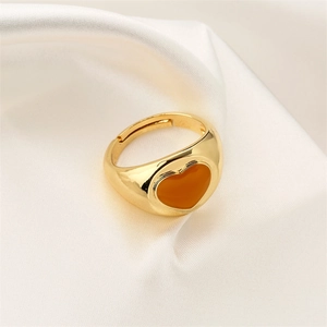 Macro shot of gold-plated heart ring with orange enamel on a soft silk background
