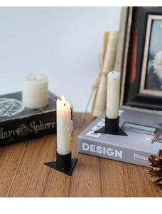 Primer plano de candelabros geométricos negros con velas blancas encendidas sobre madera