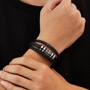 Macro detail of men's layered black leather bracelet with silver metal charms on wrist