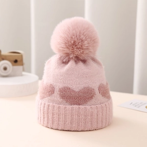 Detail of pink knitted baby hat with heart jacquard pattern and fluffy pom-pom top