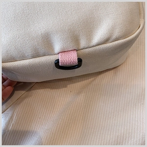 Detail of cream canvas material with pink webbing and black D-ring on children backpack
