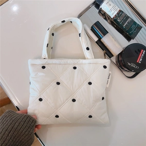 Borsa trapuntata bianca a pois neri mostrata con cosmetici su una scrivania bianca