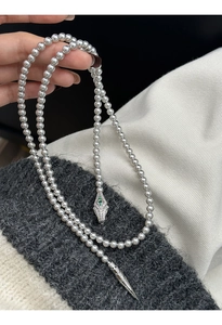 Close-up of pearl necklace featuring a serpent head clasp with green gems and zircons