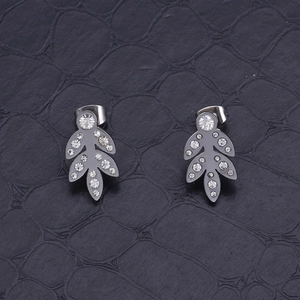 Macro shot of silver stainless steel leaf earrings with sparkling crystals on dark texture