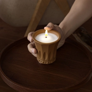 Close-up of a lit candle in a brown ceramic jar with embossed vintage patterns