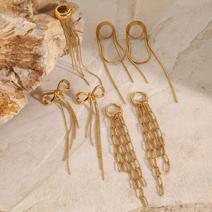 Macro shot of gold tassel earrings and bow-knot ear cuffs on a natural stone base