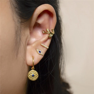 Detail of gold evil eye stud and leaf ear cuff set on model with zircon inlay