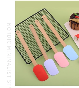 Pastel silicone spatulas with wooden handles on a cooling rack with chocolate cake