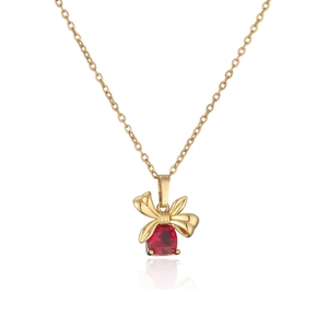 Macro detail of golden bow necklace with a central red gemstone and polished chain