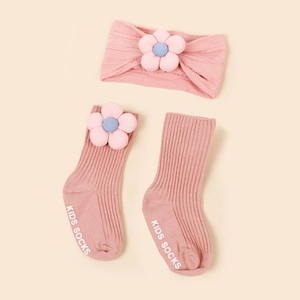 Détail de chaussettes en maille rose bébé avec fleur en tissu et bandeau assorti