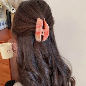 Detail einer großen Haarspange mit orangefarbenem Marmormuster in gewelltem braunem Haar
