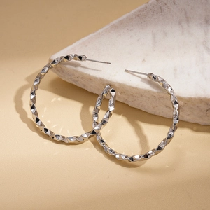 Macro shot of silver C-shaped hoop earrings with geometric facets on white stone