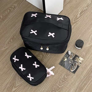 Detail of black nylon makeup bags with pink bows and elegant pearl zippers on wood floor