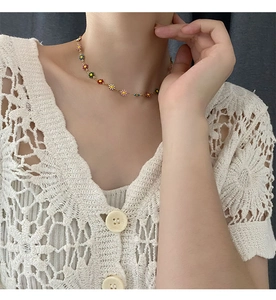 Close-up of a colorful beaded daisy pendant necklace on a gold chain worn by a model