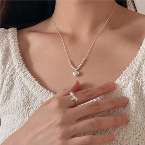 Detailed view of silver heart pendant necklace and minimalist twisted ring on model