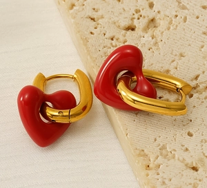 Detail of red heart pendant earrings with gold hoops on a textured stone surface