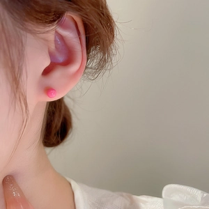 Close-up of bright pink round ball stud earrings worn by a model for a minimalist look
