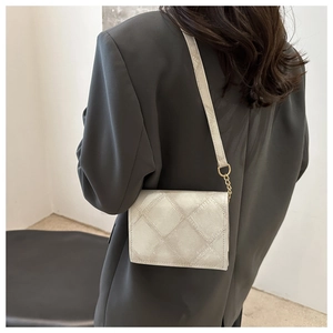 Close-up of beige quilted crossbody bag with metal chain strap on model's shoulder