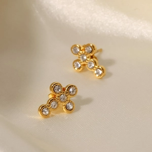 Close-up of golden cross stud earrings with sparkling cubic zirconia on beige silk cloth