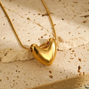 Close-up of a gold heart pendant on a snake chain over a natural stone surface