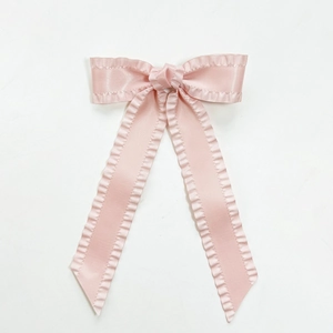 Close-up of long pink satin bow hair clip with ruffled edges and elegant ribbons