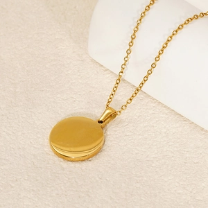 Golden stainless steel zodiac coin necklace with delicate O-chain on a beige surface