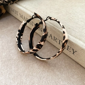 Detailed view of leopard print hoop earrings on a textured surface next to a linen book