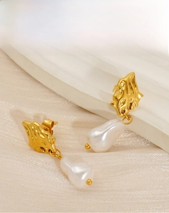 Detailed shot of gold irregular lava textured earrings with baroque pearls on a display
