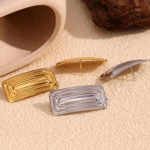 Detailed view of gold and silver rectangular pleated earrings on a textured background