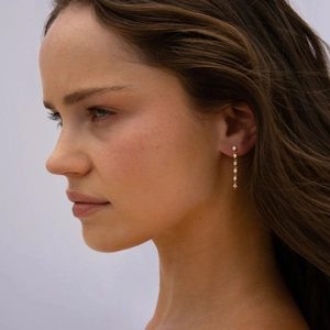 Detail of elegant gold linear drop earrings with five round cut white gemstones on model