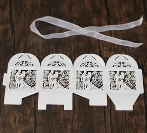 Flat lay of laser-cut white wedding candy box featuring Mr & Mrs silhouettes and ribbon