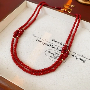 Dettaglio collana a doppio strato di perline rosse con distanziatori dorati in legno
