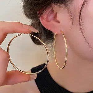 Polished gold-plated large hoop earrings featuring a minimalist circular design on a model