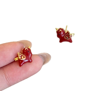 Gold plated red enamel horse stud earrings for women shown held by fingers on white background