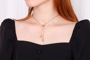 Close-up of golden stainless steel ball pendant necklace worn on a model's neck
