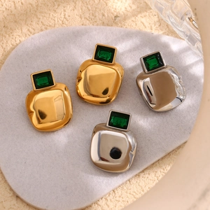 Detail of square emerald earrings in gold and silver finish on a white stone pedestal