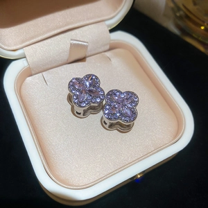 Macro shot of silver clover earrings set with purple crystals in a beige jewelry box
