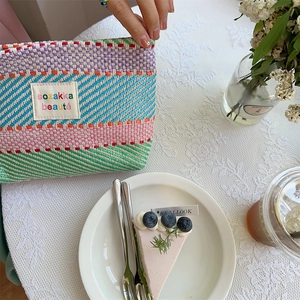 Detail of colorful striped woven toiletry bag with embroidered patch on a lace tablecloth