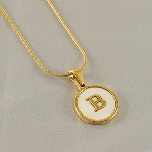 Detail of 18k gold necklace with round white shell pendant featuring a 3D letter B