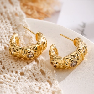 Irregular gold-plated C-shaped earrings with zircons shown on a lace fabric