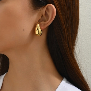 Close-up of a 18K gold teardrop earring worn by a model showcasing its glossy surface