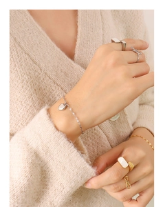 Detail shot of heart pendant bracelet and bow ring on hand with knit sweater